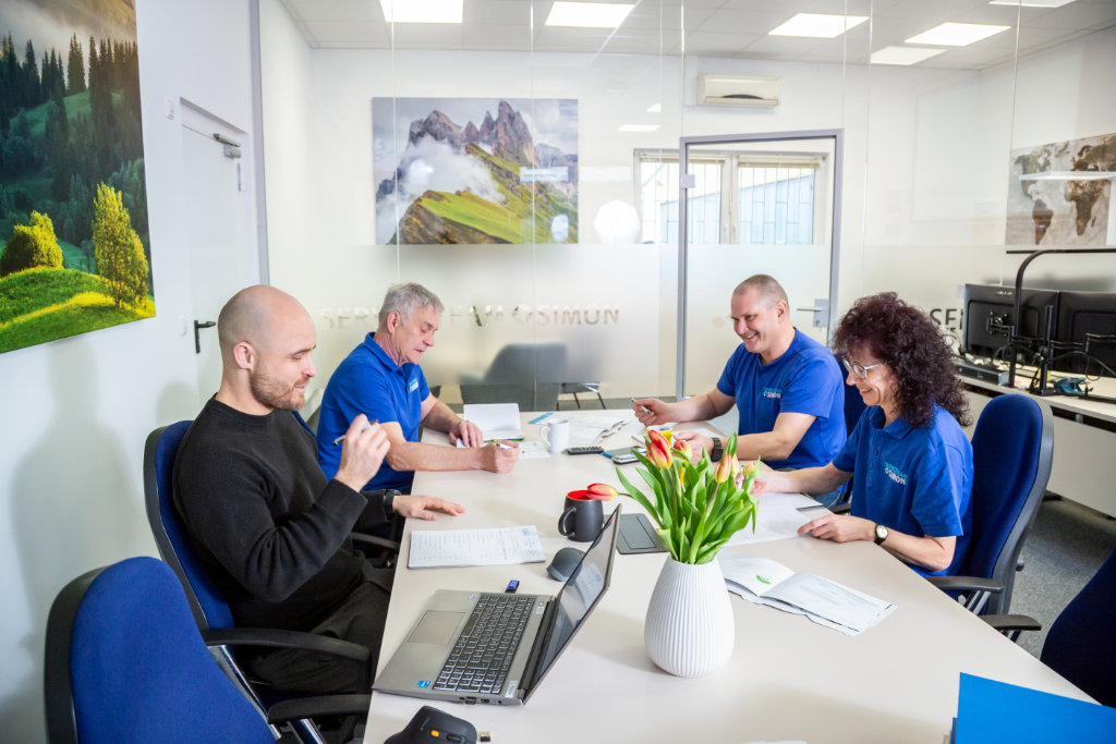 Das Service Team Simon berät sich in einem hellen, freundlichen Raum auf dem weißen Tisch befinden sich ein Laptop und Unterlagen.
