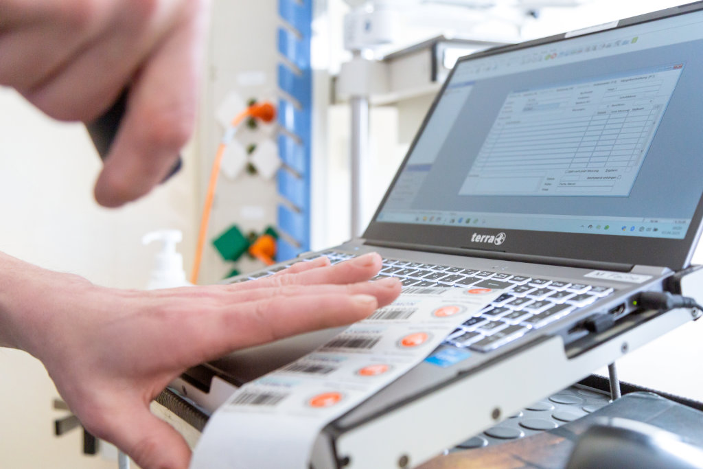 Ein Mitarbeiter vom Serviceteam Simon arbeitet am Laptop mit digitalen Formularen und Etiketten – für rechtssichere Dokumentation in der Medizintechnik.