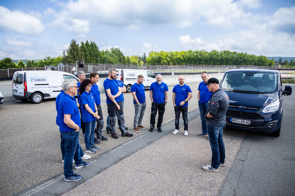Mitarbeitende vom Serviceteam Simon bei einer DEKRA-Schulung auf einem großen Gelände, Firmenfahrzeuge stehen im Hintergrund.